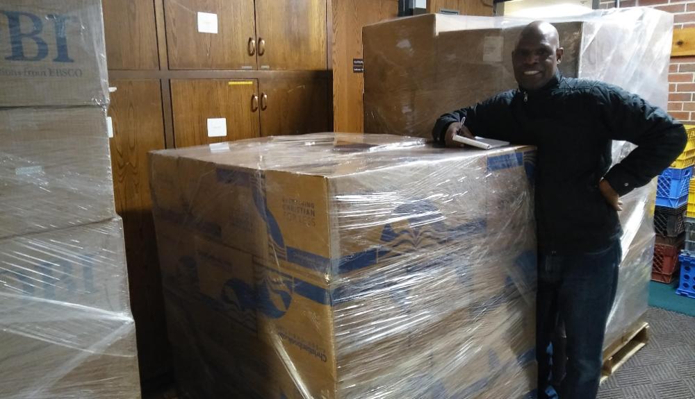 A man standing by several boxes of books