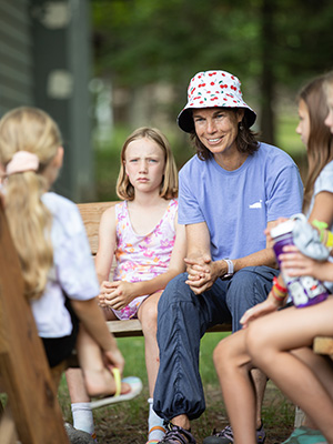 A lady sitting with a group of kids smiling