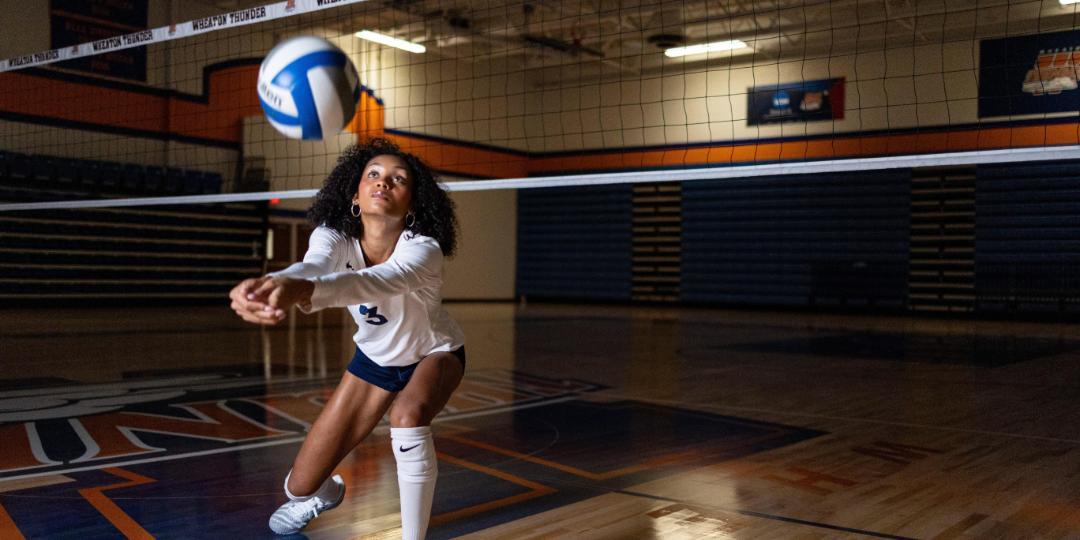 Student sets a blue and white volleyball next to a net