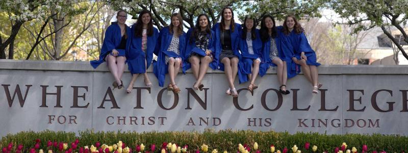 Wheaton College IL Students sitting on signs at Commencement