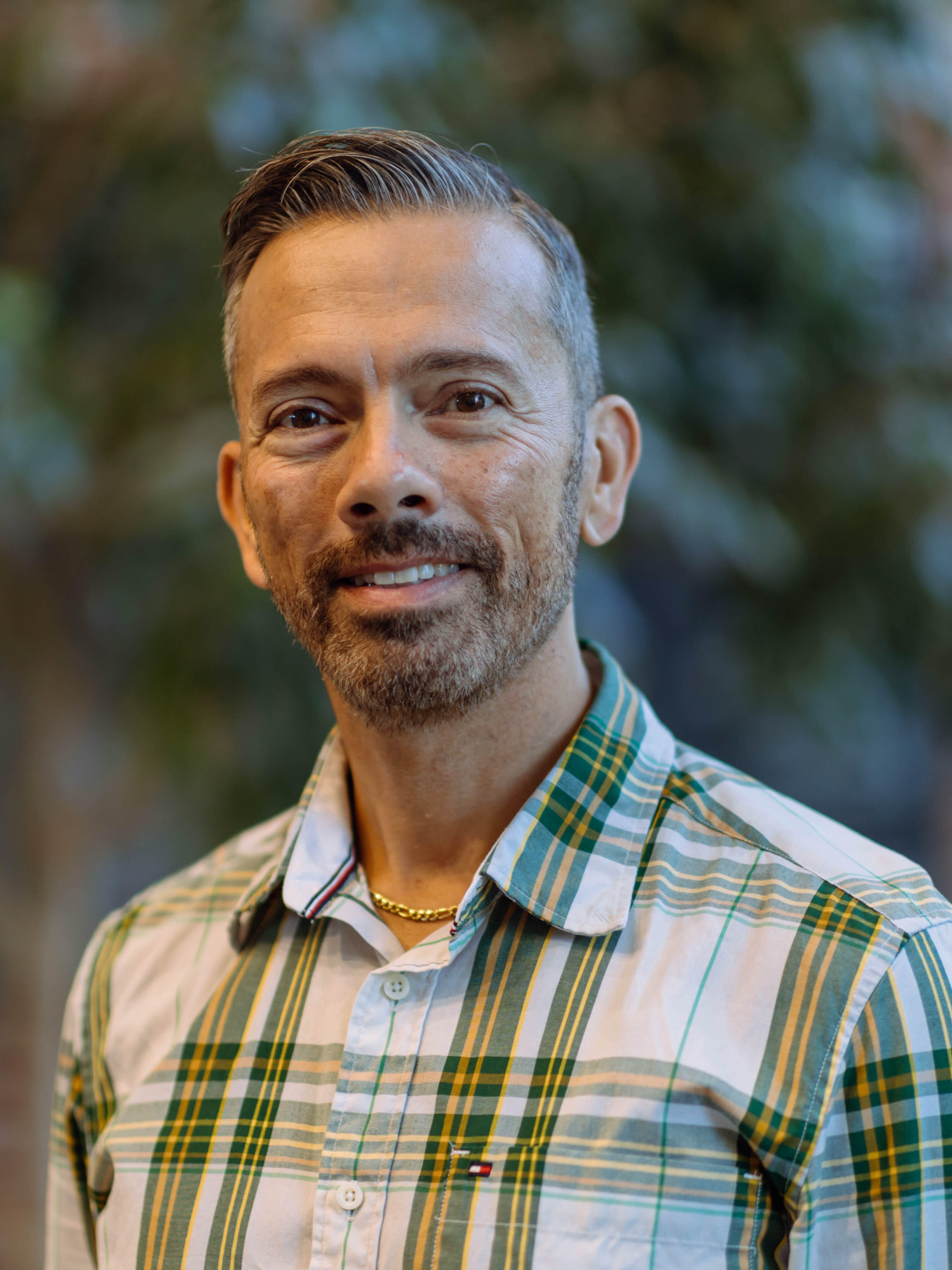 A man with a tan complexion and black and silver hair smiles