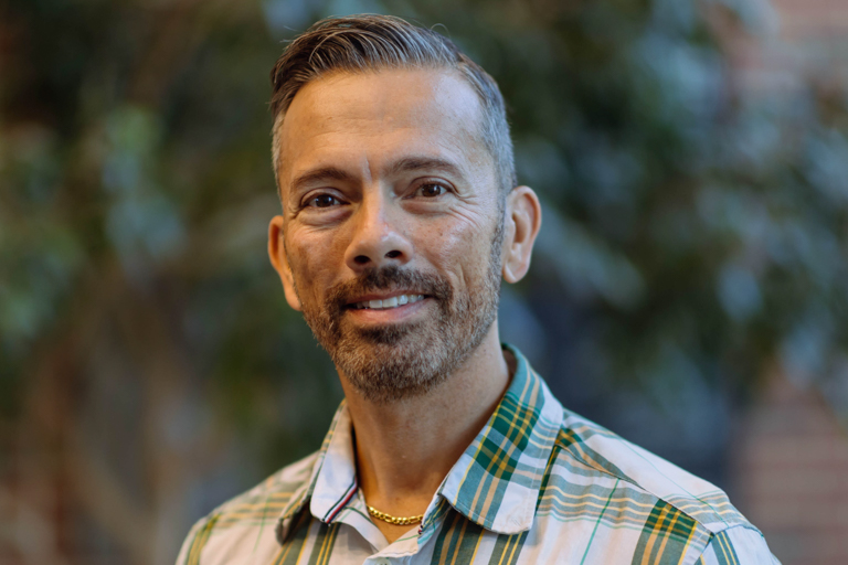 A man with a tan complexion and black and silver hair smiles