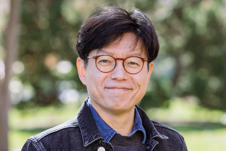 An East Asian man wearing glasses smiles