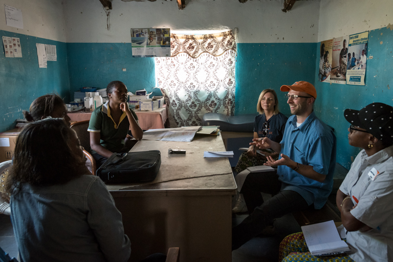 Four black women sit at a table with a white woman and a white man, who is talking.