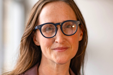 A woman with light brown hair and glasses smiles